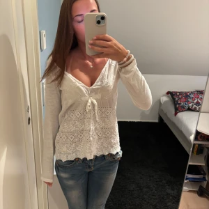Vit spetsblus med knyt och v-ringning - Supersöt vit blus med v-ringning och knyt framtill. Långa ärmar och detaljerad spets över hela framsidan ger en romantisk vibe. Perfekt till jeans eller kjol för en chill men ändå söt look.
