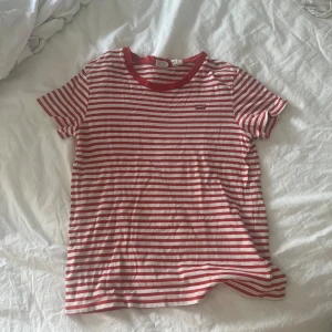 Randig t-shirt från Levi's röd/vit - Säljer en klassisk t-shirt från Levi's med röda och vita ränder. T-shirten har rund halsringning med röd kant och korta ärmar. Perfekt basic-plagg med liten Levi's-logga på bröstet. Tillverkad i mjuk bomull för skön känsla.