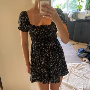 Svart byxdress med vita prickar - Supersöt svart byxdress med vita prickar och puffärmar. Klänningen har smockad midja, volangkant nertill och kan bäras både med puffärmarna uppe eller offshoulder. Perfekt för sommardagar💗