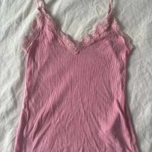 Rosa linnetopp med spetsdetaljer - Supersöt rosa linnetopp i skönt material med tunna axelband och v-ringning. Toppen har fina spetsdetaljer längs urringningen. Köpt från New Yorker och kommer inte mer till användning. Kontakta gärna innan köp!
