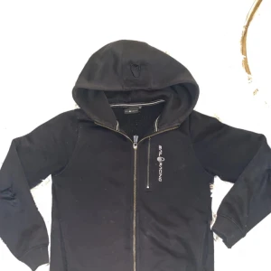Svart hoodiejacka från Sail Racing - Svart hoodiejacka från Sail Racing med dragkedja framtill och huva. Möts upp för lämning oftast i Sthlm