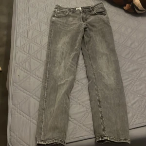 Grå raka jeans i tvättad denim - Säljer ett par grå jeans med tvättad look och raka ben. Klassisk femficksmodell med snygga kontrastsömmar och metallnitar. Jeansen har normal passform och är tillverkade i slitstark denim. Perfekta för dig som gillar en avslappnad stil. Den har används rätt så mycket och är därför lite sliten men det går att fixas när man köper den