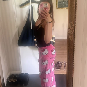 Hello Kitty rosa mjukisbyxor - Supergulliga rosa mjukisbyxor med Hello Kitty-motiv över hela byxorna. De är fluffiga och har resår i midjan för extra komfort. Perfekta för chill dagar hemma eller sleepovers. Byxorna har en loose passform och är riktigt mjuka mot huden.