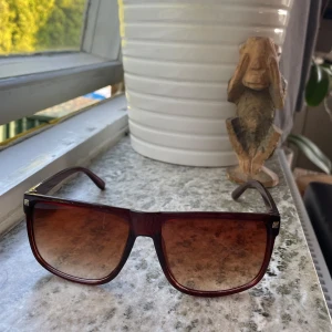 Bruna solglasögon - Snygga solglasögon med fyrkantig form och brun transparent båge. Glasen är tonade i brunt och ger en cool retrovibe. Perfekta för att lyfta din stil under soliga dagar. Lätta och bekväma att bära.