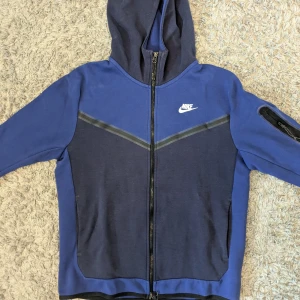 Blå Nike Tech- fleece - Nike tech- fleece i två nyanser av blått med hel dragkedja och huva. Tröjan är i fint skick och pris kan diskuteras!