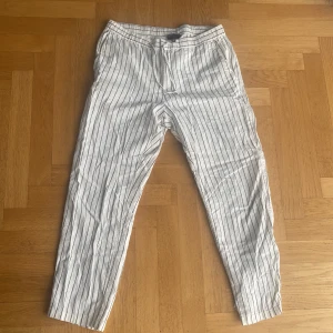 Randiga linnebyxor från H&M, M - Snygga vita linnebyxor från H&M i regular fit med svarta vertikala ränder. Byxorna har elastisk midja och sidfickor, perfekta för en chill och stilren look. Lätta och luftiga, passar grymt till sommaren.