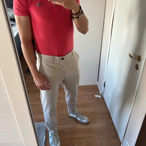 Lacoste piketröja  - Snygg röd pikétröja från Lacoste med klassisk krage och half zip-dragkedja framtill. Ikoniska krokodilloggan broderad på bröstet. Tröjan är kortärmad och gjord i mjuk bomull, perfekt för en clean och sportig look.