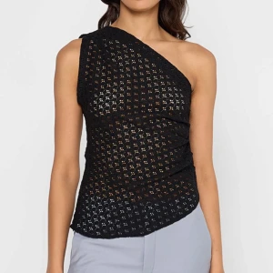 Svart oneshoulder topp från Mango - Svart oneshoulder topp från Mango i broderad bomull med genombrutet mönster. Snygg asymmetrisk skärning och figurnära passform. Cool och trendig topp! Mycket bra skick, använd cirka två gånger!