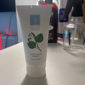 Raunsborg Hand Cream Nordic 50ml - Handkräm från Raunsborg i en vit tub med grön växtillustration. Innehåller 50 ml och passar alla hudtyper. Krämen är lätt och absorberas snabbt, med ingredienser som gurka, aloe vera och lindextrakt. Perfekt att ha i väskan för mjuka händer.