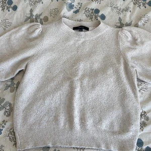 Beige stickad tröja Vero Moda puffärm - Superfin beige stickad tröja från Vero Moda med puffärmar och ribbade muddar. Tröjan har en rund halsringning och är i mjukt material som känns skönt mot huden. Perfekt för lager-på-lager och snygg till både jeans och kjol.