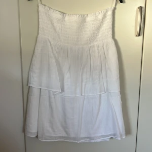 Vit tubklänning i bomull - Superfin vit tubklänning från Gina Tricot i luftig bomull. Klänningen är kort, har smock upptill och tunna axelband. Perfekt för varma sommardagar med sin lätta och flowiga känsla. Enkel och stilren design som är lätt att matcha.