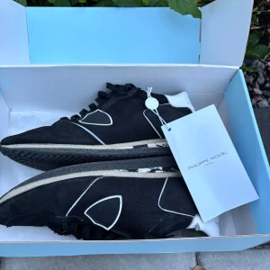 Svarta sneakers från Philippe Model STORLEK 41 - Svarta Philippe Model sneakers med vita detaljer och logga på sidan. Skorna har snörning, vit hälkappa och platt sula. Materialmix av textil och skinn ger en sportig och stilren vibe. Perfekta för dig som gillar streetstyle och vill ha något unikt på fötterna.