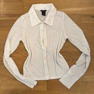 Vit ribbad skjorta från Lindex XS - Vit skjorta från Lindex i storlek XS. Skjortan har lång ärm, klassisk krage och knäppning framtill. Materialet är ribbat bomullstyg med diskreta ränder som ger en snygg struktur. Perfekt till jeans eller kjol för en clean look. Man kan även öppna knapparna och göra det till en kofta. Den är lite mindre i storleken. 💕