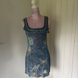 Blå kortklänning med motiv - Blå kort nyårsklänning. Glittrar fint i ljuset, kort slit på sidan. Nypris 800