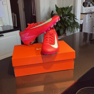 Nike air zoom mercurial vapor 16 pro fg mad energy - Splitternya fotbollsskor från Nike i en stark rosa färg med turkosa detaljer och stor turkos swoosh på sidan. Skorna har snörning, låg profil och mönstrad sula med dobbar för bra grepp på planen. Tillverkade i syntetmaterial för lätt känsla och snabbhet. Storlek 44