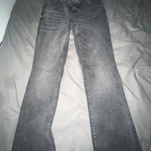 Grå bootcut jeans från H&M Divided - Snygga grå jeans från H&M Divided med bootcut passform. Jeansen har klassisk femficksdesign, dragkedja och knapp framtill samt coola detaljer på bakfickorna. Perfekta för dig som gillar en avslappnad men trendig look.