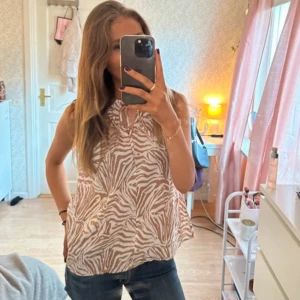 Beige och vit zebramönstrad  blus - Säljer en luftig ärmlös blus med beige och vitt zebramönster. Toppen har en liten knytning vid halsen. Säljer för att jag ska flytta och behöver rensa garderoben!