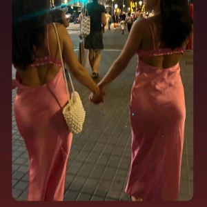 Rosa långklänning med öppen rygg - Snygg rosa långklänning med smala axelband och öppen rygg. Klänningen har en elegant passform och är perfekt för somriga tillfällen. Den har en knytning framtill som ger en extra detalj.