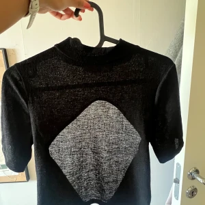 Svart croppad bolerotopp från NA-KD - Säljer en svart croppad topp från NA-KD. Toppen har korta ärmar, hög hals och en öppen rygg med knytning nedtill. Perfekt att styla över linnen eller klänningar för en trendig look.