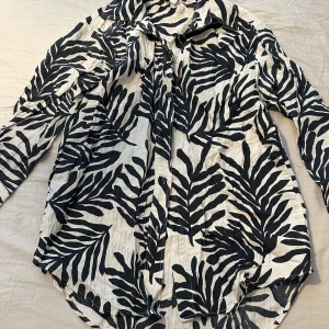 Svartvit mönstrad skjorta från H&M - Säljer en svartvit skjorta från H&M med ett stort, grafiskt zebramönster. Skjortan har långa ärmar, klassisk krage och knäppning framtill. Perfekt för dig som vill sticka ut med ett coolt mönster.