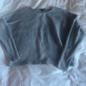Grå stickad tröja - Säljer en enkel och stilren grå stickad tröja med rund halsringning. Tröjan har lång ärm och rak passform, perfekt för lager-på-lager. Materialet är mjukt och ger en avslappnad känsla.