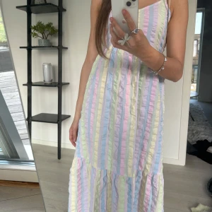 Pastellrandig långklänning med smala axelband - Säljer en söt långklänning med smala axelband och v-ringning. Klänningen har pastellfärgade ränder i ljusa toner och en luftig, flowy passform. Perfekt för varma dagar och sommarens alla tillfällen.