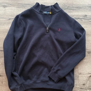 Ralph Lauren tröja - Mörkblå långärmad tröja från Polo Ralph Lauren med halv dragkedja och röd broderad logga på bröstet. Klassisk och stilren modell med ribbade muddar vid ärmslut och nederkant. Helt ny endast använd en gång. Skicka Pm vid minsta fundering