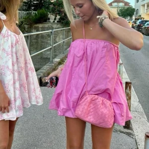 Rosa axelbandslös kortklänning - Söt rosa axelbandslös kortklänning med luftig passform och volangliknande kjol från Zara. Perfekt för varma dagar och enkel att styla med accessoarer. Klänningen har tunna axelband och en avslappnad siluett.