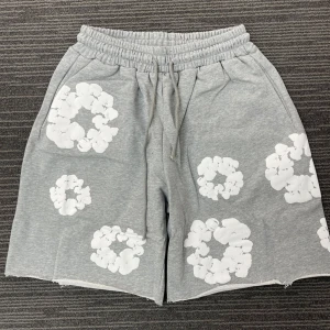 Grå Denim Tears shorts - Grå shorts med elastisk midja och snörning. Dekorerade med stora vita blommönster över hela plagget. Mjukt material och avslappnad passform, perfekta för varma dagar.