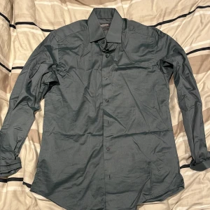 Mörkgrå skjorta från Dressmann - Säljer en stilren mörkgrå skjorta från Dressmann i slim fit-modell. Skjortan är långärmad, har klassisk krage och knäppning framtill. Tillverkad i premium bomull för en skön känsla och snygg passform.