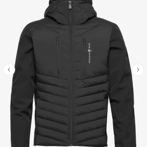 Svart pufferjacka från Sail Racing - Svart pufferjacka från Sail Racing med huva och dragkedja framtill. Jackan har två bröstfickor med dragkedja och diskret logga på bröstet. Snyggt mönstrad med horisontella paneler och en sportig look. Perfekt jacka för sommar kvällar! Skriv om ni har några funderingar!