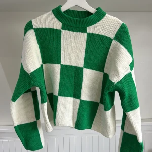 Grön och vit rutig stickad tröja från Gina Tricot - Säljer en stickad tröja från Gina Tricot i storlek XS. Tröjan har ett grönt och vitt rutigt mönster, rund halsringning och långa ärmar. Perfekt för dig som gillar färg och mönster!