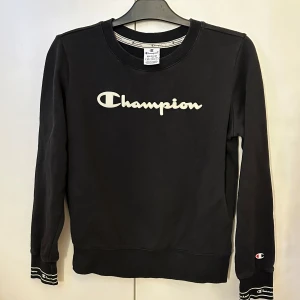 Svart sweatshirt från Champion - Säljer en svart sweatshirt från Champion med klassisk logga framtill och detaljer vid ärmslut. Tröjan har rund halsringning och långa ärmar. Passar även om man har storlek S. Använd fåtal gånger. 