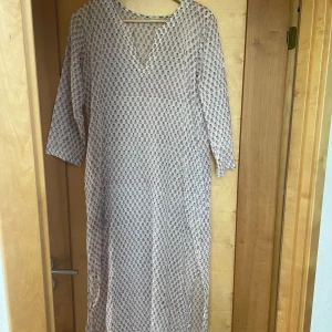 Blommig långklänning från Picok - Luftig långklänning/nattlinne från Picok i vitt med små blommiga mönster i rött och blått. Klänningen har v-ringning och trekvartsärm, perfekt för varma dagar. Tillverkad i tunn bomull som känns sval och skön. Varan är aldrig använd men saknar prislapp 