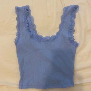 Ljusblå ribbad linnetopp med spets från Clockhouse - Supersöt ljusblå ribbad linnetopp från Clockhouse med breda axelband och fina spetsdetaljer längs kanterna. Perfekt att styla till jeans eller kjol för en fräsch look.