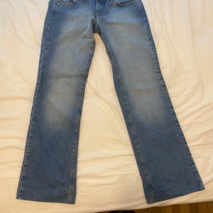 Vintage baggy jeans - Säljer ett par blå baggy jeans med breda ben och cool rosa text 'RICH' på bakfickorna. Jeansen har klassisk femficksdesign och normal passform. Perfekta för dig som vill sticka ut lite extra!