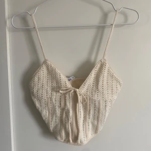 Beige stickad croppad linnetopp från Zara - Säljer en beige stickad linnetopp från Zara med smala axelband och knyt framtill. Toppen är croppad och har ett snyggt virkat mönster som ger en somrig känsla. Perfekt att matcha med jeans eller kjol!