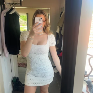 Vit virkad klänning från Zara - Superfin vit virkad klänning från Zara med kort ärm och fyrkantig ringning. Klänningen har ett vackert hålmönster och är lätt utsvängd nertill. Perfekt för sommarens alla tillfällen! Säljes i storlek XS.