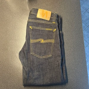 Mörkblå jeans från Nudie Jeans - Tja. Säljer ett par mörkblå jeans från Nudie Jeans med klassisk orange söm och Nudie-logga på bakfickan. Jeansen har raka ben och fem fickor. Perfekta för dig som gillar stilrena och tidlösa jeans. Går med på prisförslag vid rätt pris! Tveka inte att höra av dig vid funderingar 🤩😊