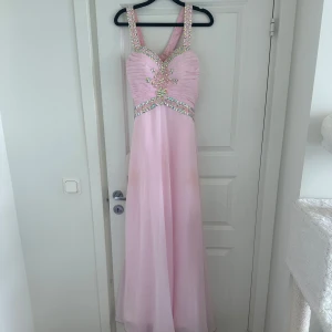 Balklänning rosa med strass  - En rosa jättefin balklänning med strass på. Den är sydd  men har ingen lapp, skulle säga den passar XS/S. Den har fläckar av brun utan sol på, har inte testat att ta bort dom. 
