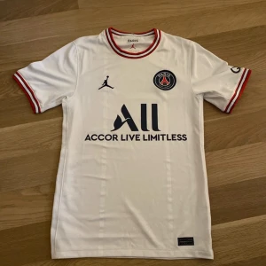Vit PSG fotbollströja från Jordan - Säljer en vit PSG fotbollströja från Jordan med röda och blå detaljer på krage och ärmslut. Tröjan har klubbmärke på bröstet, sponsortryck och Jordan-logga. Tillverkad i lätt och ventilerande material. Passar ungefär 165-175. Tröjan är helt äkta!