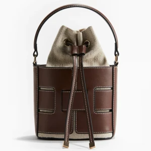 Brun och beige bucket bag med snörning - Snygg bucket bag i brunt skinn och beige canvas med dekorativa sömmar och snörning upptill. Väskan har både handtag och avtagbar axelrem för olika stilar. Perfekt accessoar för dig som vill sticka ut.