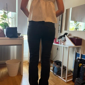 Svarta  lådmidjade jeans med normal passform - Säljer ett par svarta jeansbyxor med klassisk femficksdesign och raka ben. Byxorna har normal passform och stängs med dragkedja och knapp. Perfekta till många olika outfits och enkla att matcha.