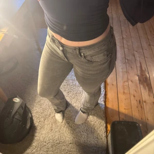 Grå jeans med bootcut - Säljer ett par grå jeans med bootcut-modell och råa, fransiga benslut då jag tog bort den nedre sömmen. Jeansen har klassisk femficksdesign, dragkedja och knapp framtill. Snygg tvätt och passar perfekt till en avslappnad stil.