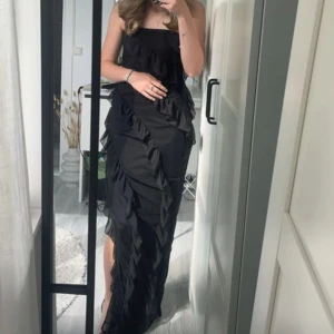 Svart långklänning med volangdetaljer - Inte min bild! Säljer denna svarta långklänning med volanger.  Klänningen är axelbandslös och är Perfekt för bal och andra festliga tillfällen❤️