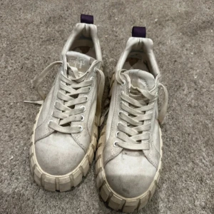 Vita sneakers från Eytys med chunky sula - Säljer ett par vita sneakers från Eytys med kraftig, chunky sula och lila hälflik. Skorna har snörning och är tillverkade i textilmaterial. Perfekta för dig som gillar en unik och trendig stil.