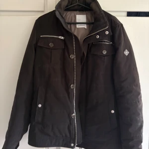 Svart jacka från J.Lindeberg - Säljer en svart jacka från J.Lindeberg med dragkedja och knappar framtill. Jackan har flera fickor med både dragkedja och knappar samt en hög krage. Perfekt för kyligare dagar.