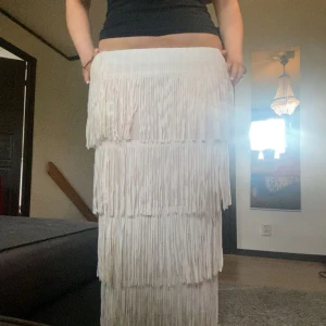 Vit långkjol med fransar - Säljer en vit långkjol med flera lager fransar som ger en riktigt cool och bohemisk vibe. Kjolen har rak passform och är perfekt för dig som vill sticka ut med en unik look. Superfin att styla med en enkel topp eller crop. Fick i present så vet inte vart den är ifrån, aldrig använd endast provad. Står ingen storlek men jag bär vanligtvis M och finns resårband så passar större också! Krämvit färg, den är även lite genomskinlig (se sista bilder). Lägg gärna prisförslag 