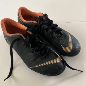 Nike Mercurial fotbollsskor svart/orange - Säljer ett par Nike Mercurial fotbollsskor i svart med orange detaljer och innersula. Skorna har snörning och är designade för bra grepp på planen. Perfekta för dig som vill ha stilrena och lätta fotbollsskor.