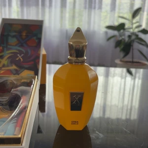 Erba Gold parfym från Xerjoff - Lyxig parfymflaska i klargul färg med guldfärgat metallock och dekorativ etikett framtill. Kommer i en färgstark, mönstrad förpackning som ger exklusiv känsla. Doften heter Erba Gold och flaskan har en elegant, modern design.